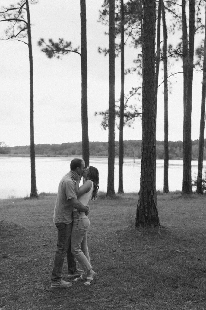 A man and woman embracing and kissing in the woods with water in the background