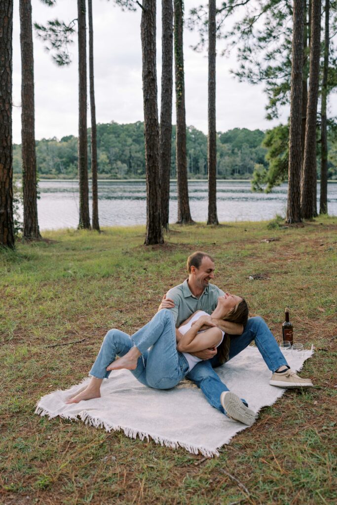 A man and woman laying on the ground on a woven blanket, he is embracing her, and they are laughing. 