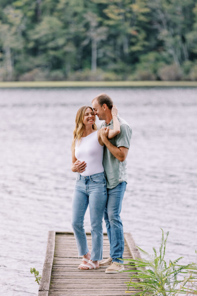 A man and woman embracing on a dock with water and trees in the background 