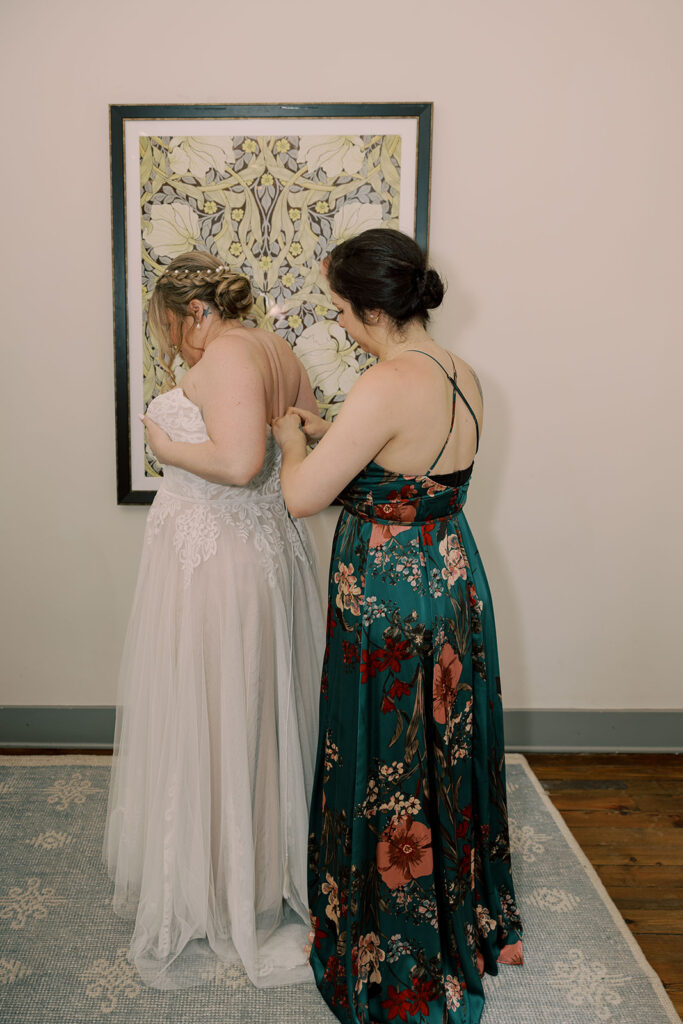 sister of the bride helping her with her wedding dress